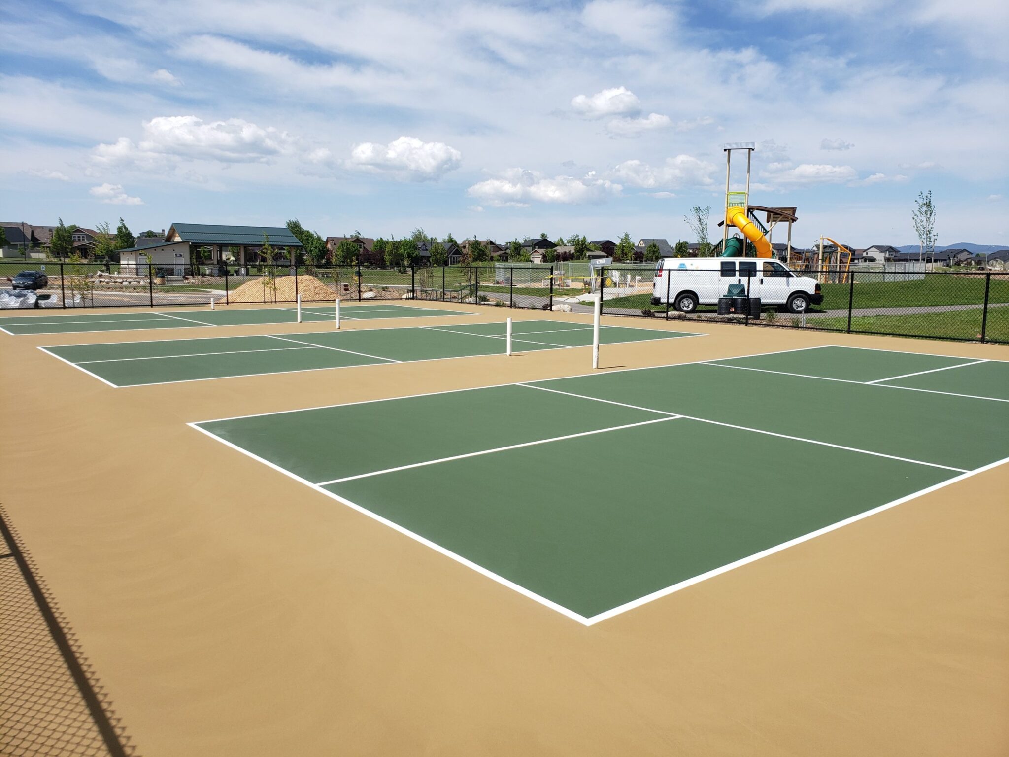 A newly surfaced set of three pickleball courts with green, white, and tan colors