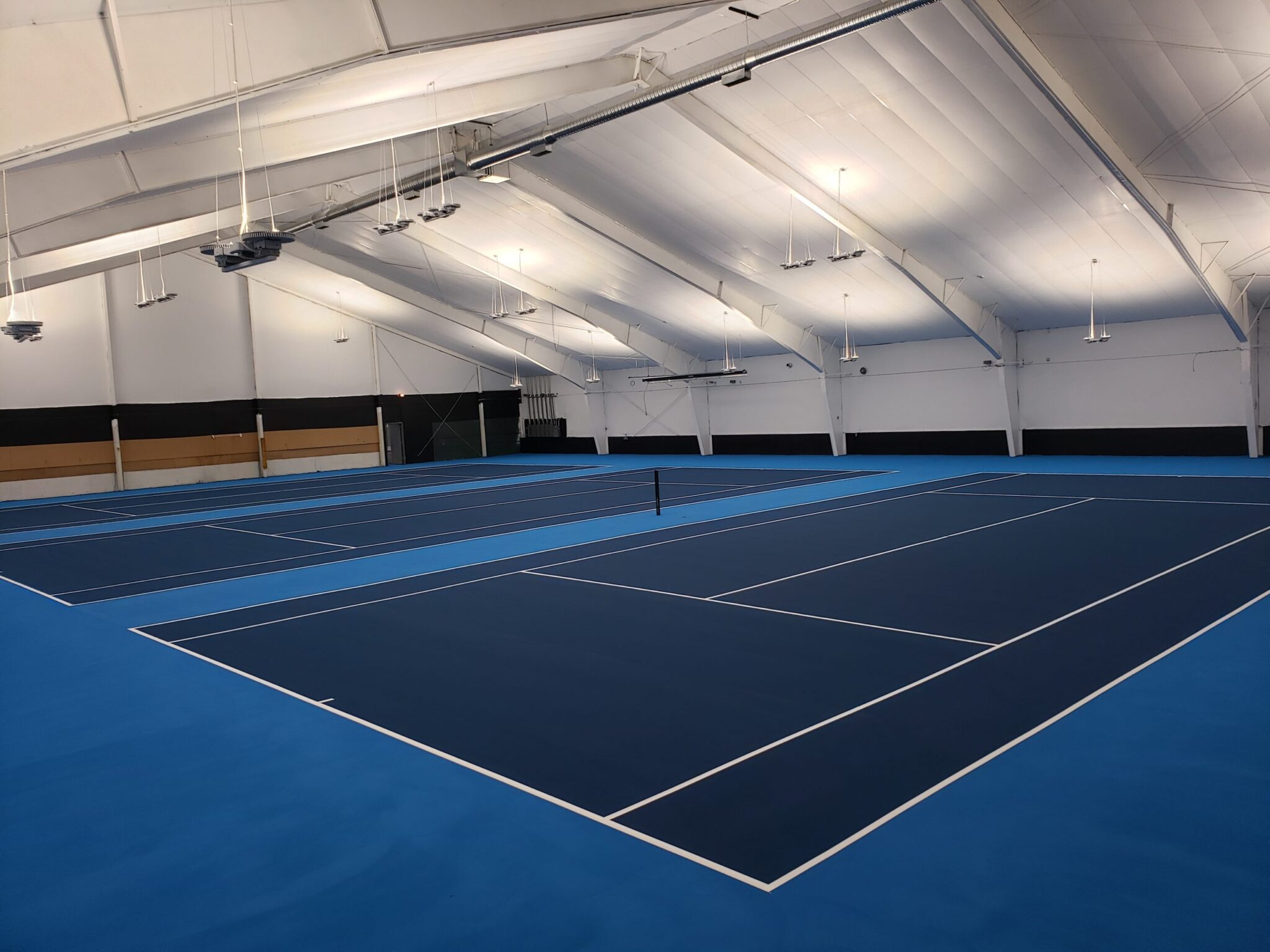Three indoor tennis courts next to each other with blue and white colors.