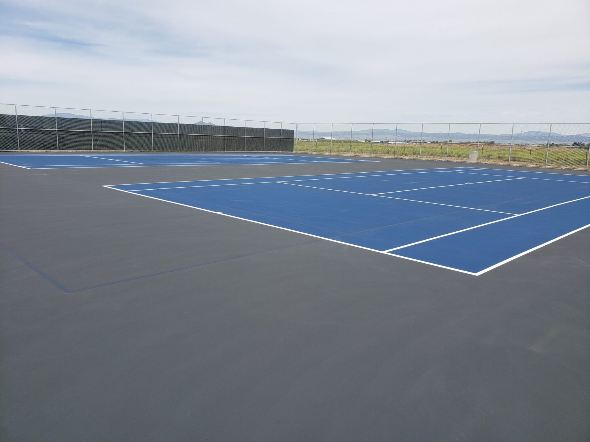 A new tennis court complex with fencing that includes grey, blue, and white colors.