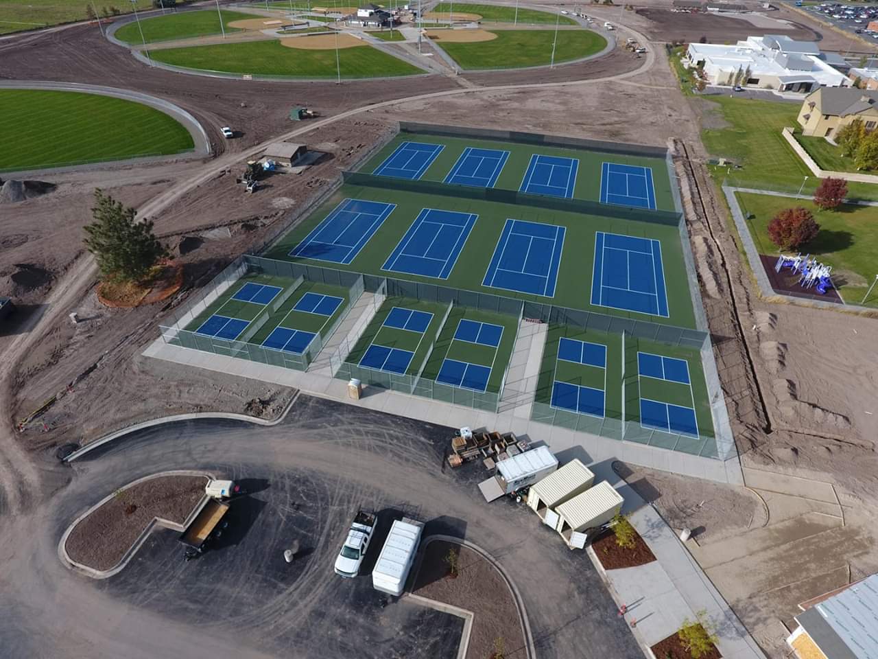 An aerial view of a brand new tennis and pickleball complex with fencing and green, blue, and white colors.