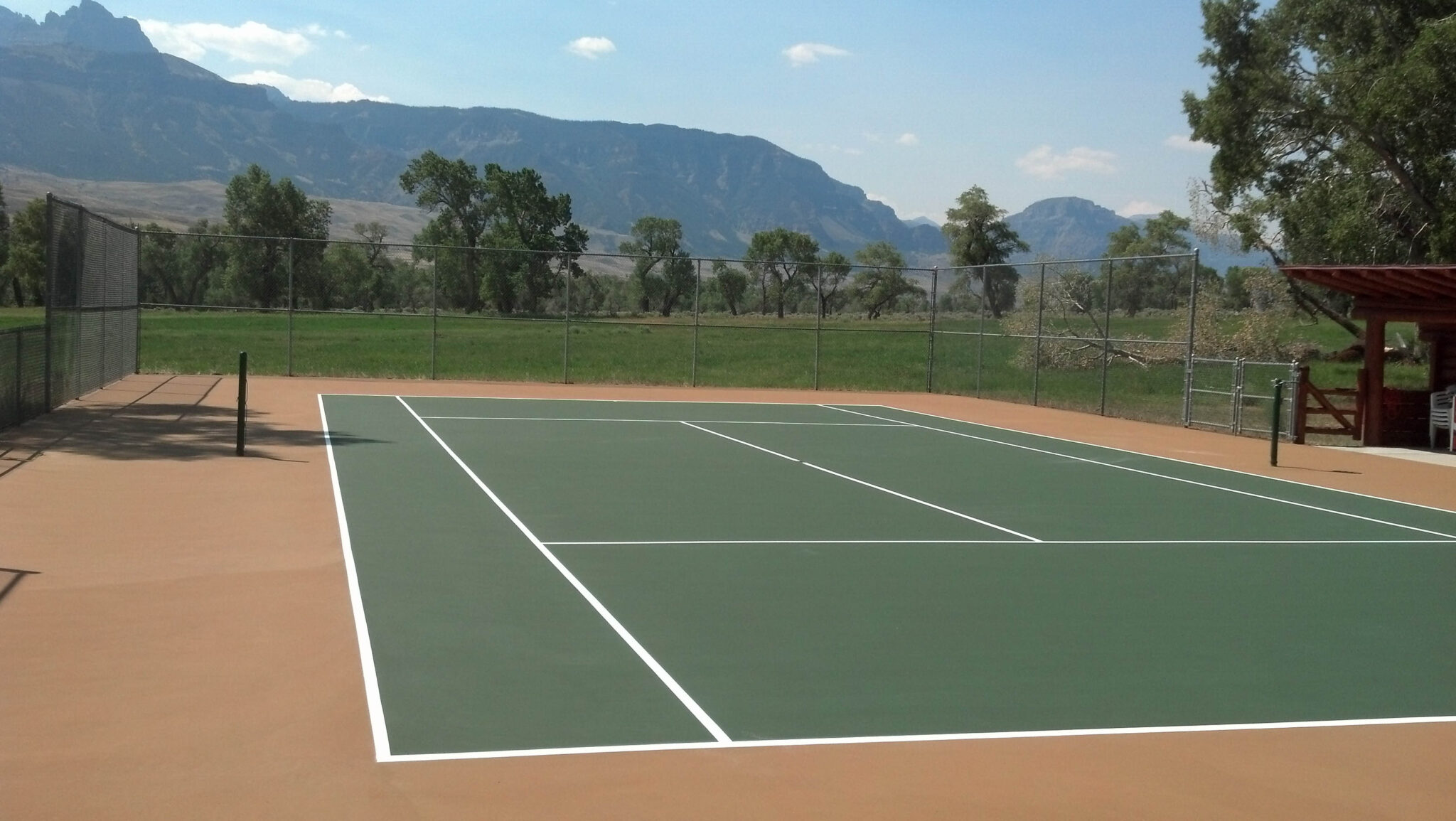 A new tennis court with big mountains in the background a green, white, and tan color scheme.