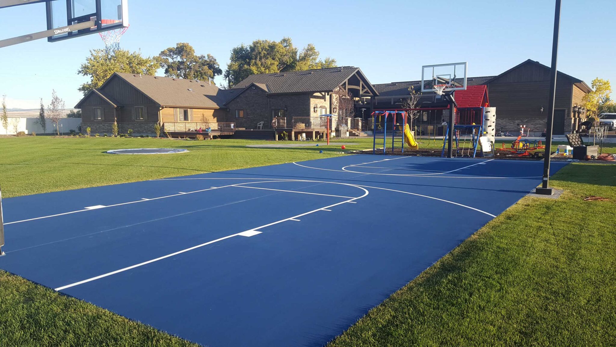 A newly surfaced basketball court in a backyard with blue and white lines.