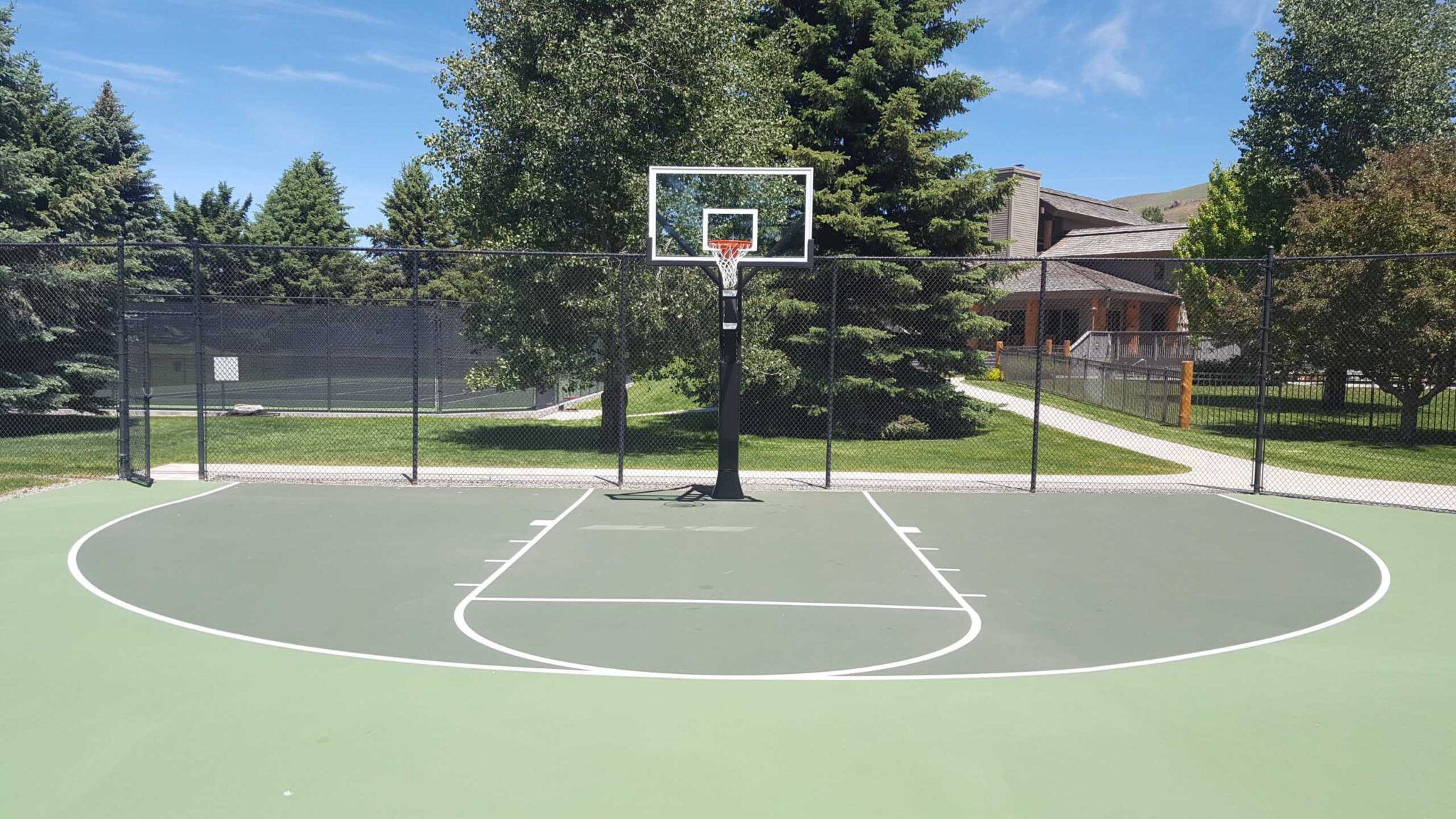 A new half-court basketball surface with fencing and a green and white color sheme.