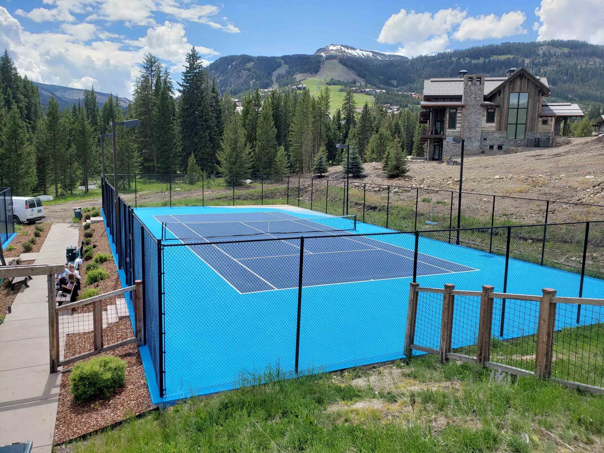 A new tennis court including a blue and white color scheme backdropped by luxury homes and mountains.
