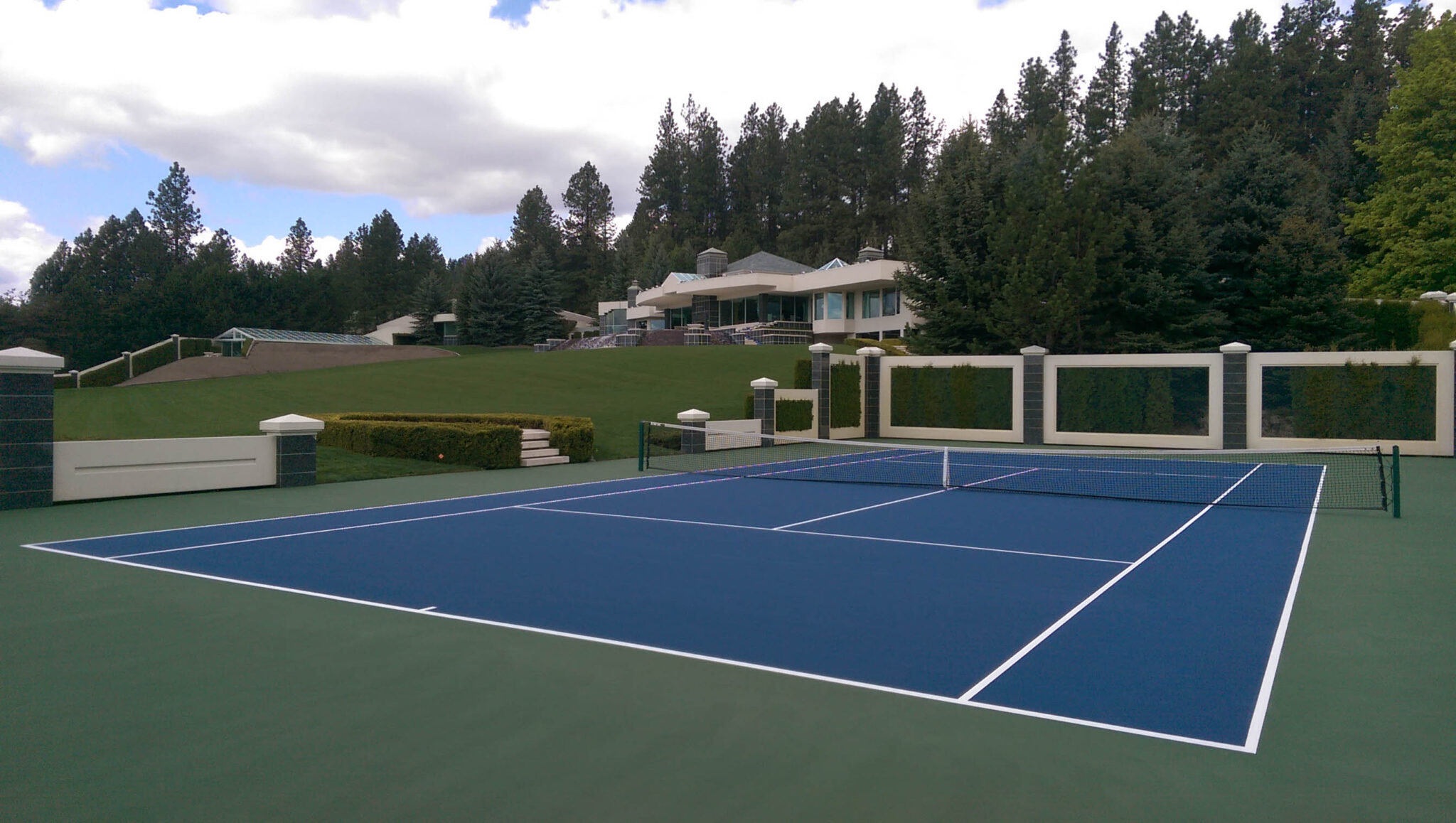 A new tennis court in a backyard with nice fencing and a court color scheme of green, blue, and white.